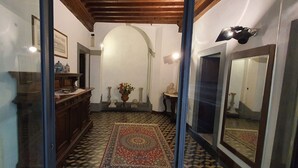 Ein schmales Entree mit Teppichmuster, einer Holzbank, einer Vase mit Blumen und einem Spiegel an der rechten Wand.