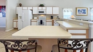 Une cuisine moderne avec des meubles blancs, un îlot central et un coin repas équipé de deux chaises.