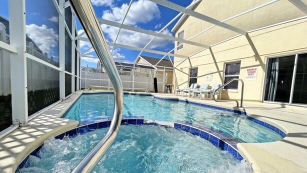 Une piscine avec un espace jacuzzi, entourée d’une terrasse couverte et d’un bâtiment doté de grandes fenêtres.