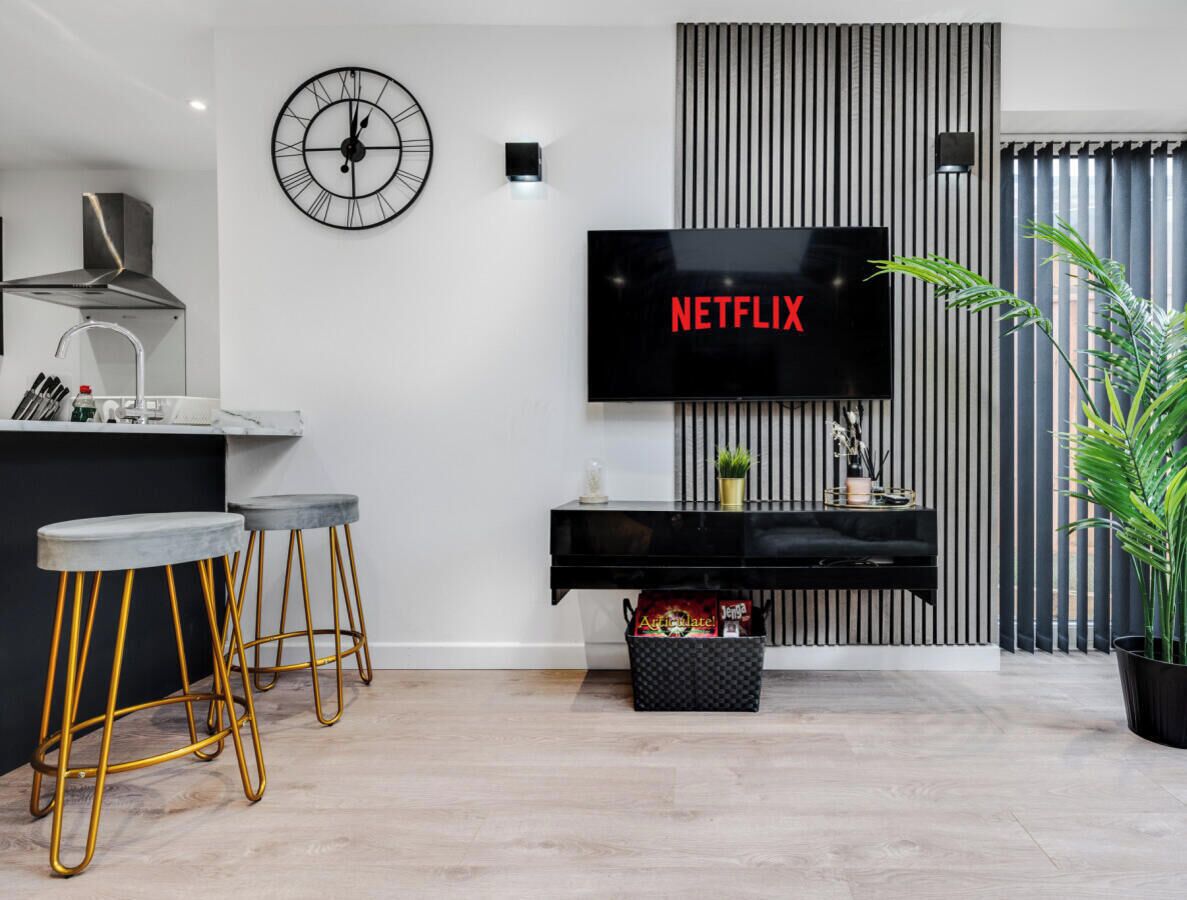 A modern kitchen with a built-in stove, a bar area with stools, a wall-mounted TV displaying 'NETFLIX,' and a potted plant.