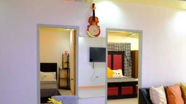 A room with a bed, a desk, a chair, a TV, and a violin on the wall. - Tranquil Retreat: Inviting 2BR Condo in Zamboanga (Zamboanga)