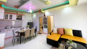 A modern kitchen with white cabinets and a dining area with a black sofa and yellow cushions. - Tranquil Retreat: Inviting 2BR Condo in Zamboanga (Zamboanga)