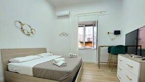 Un dormitorio moderno con cama, escritorio con silla, televisión y vistas al balcón.