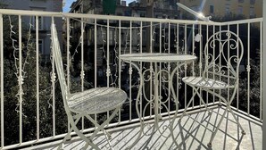 Un balcón con baranda de metal, dos sillas de metal y una mesita.
