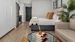 A modern hotel room with a bed, a sofa, a glass coffee table, and a potted plant. - Modern Studio On Bree Street (Cape Town)