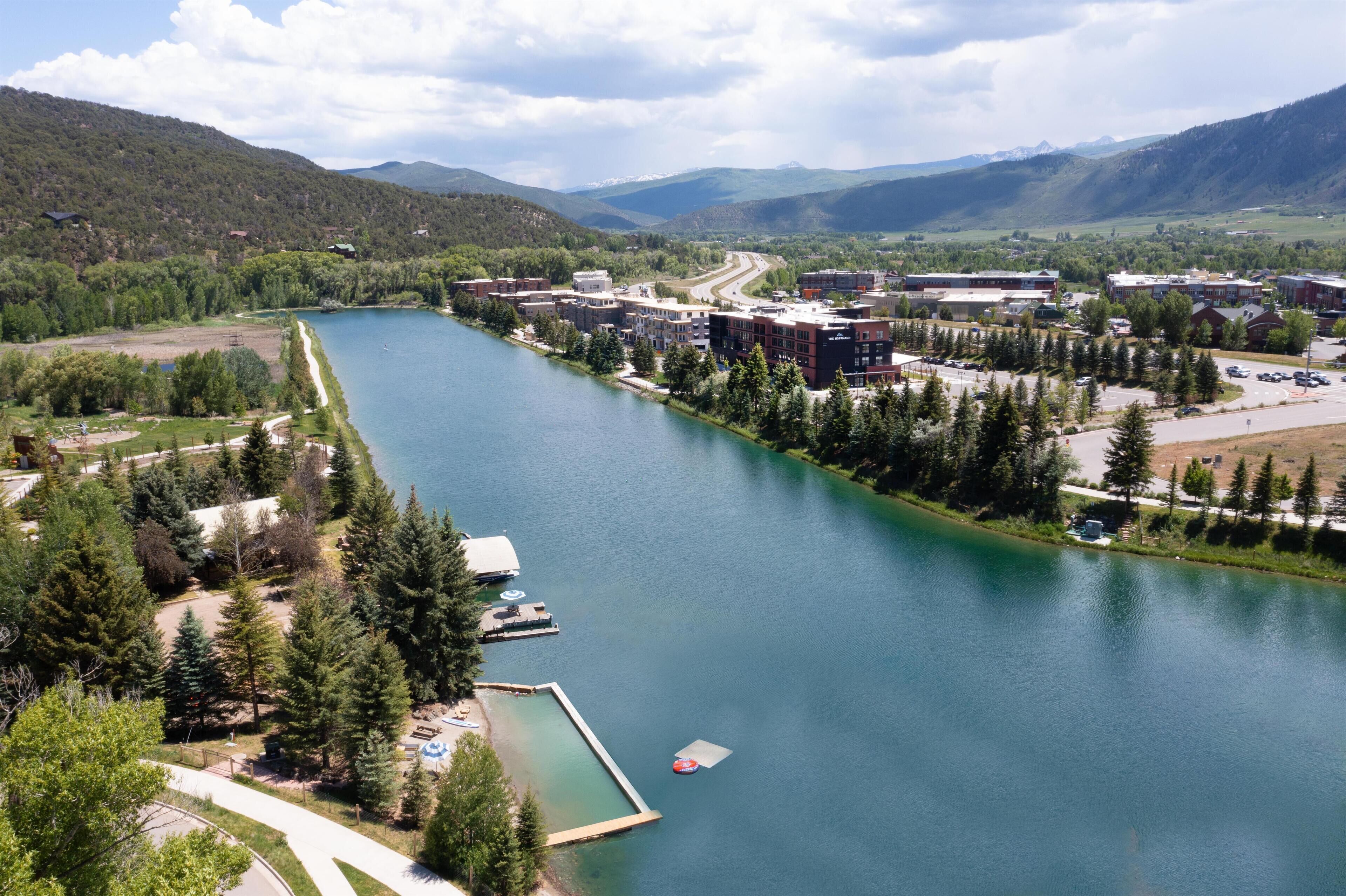 A lakeside view of a town with buildings, a dock, and a road leading into the distance.