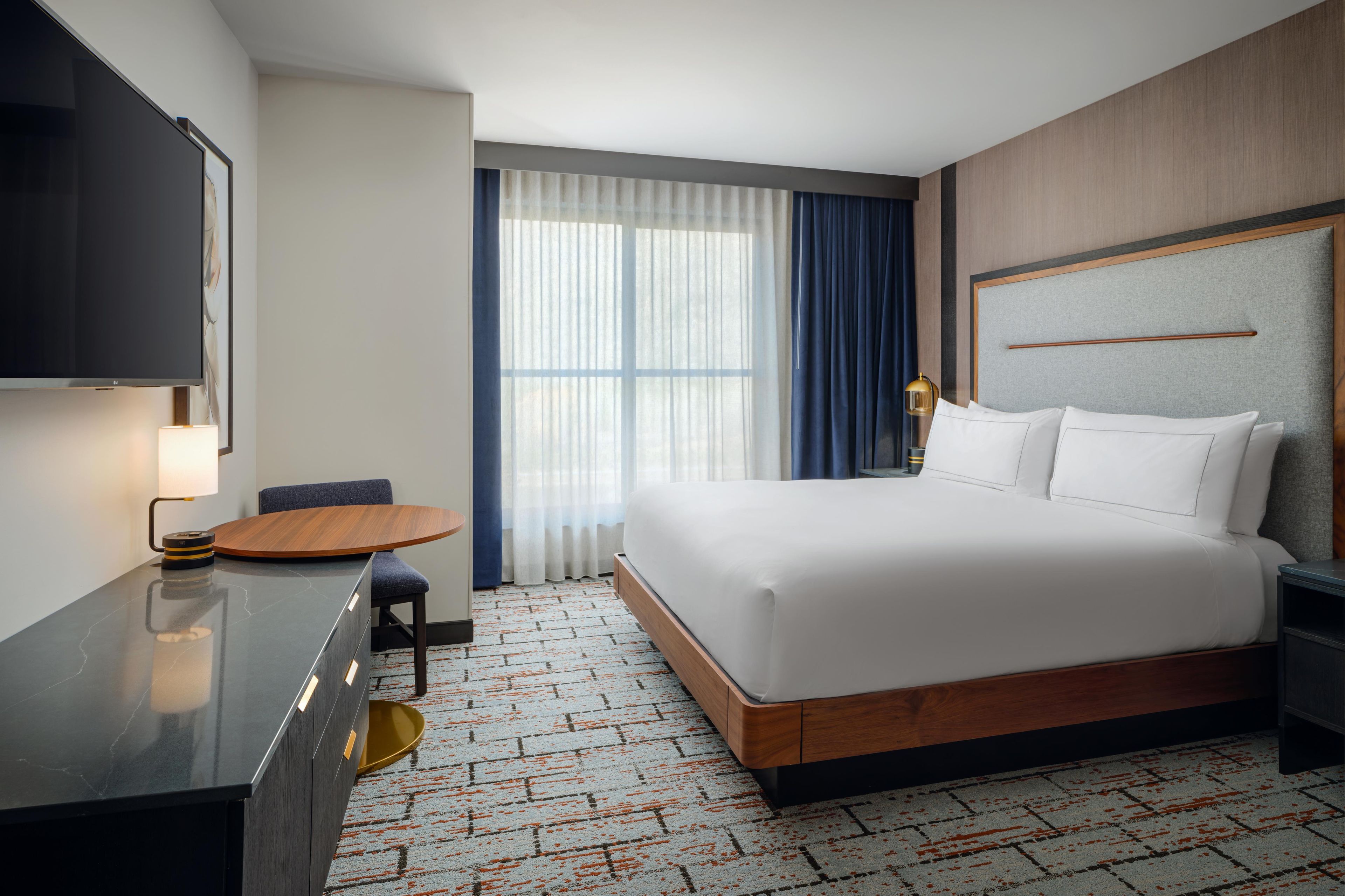 A hotel room with a bed, a desk, a chair, a television, and a window with curtains.