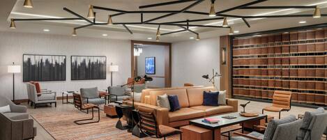 A modern hotel lobby with a central seating area, a bookshelf, and a large window.