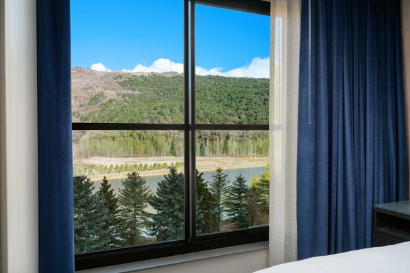Una habitación con un ventanal que ofrece vistas a un lago, árboles y una montaña.