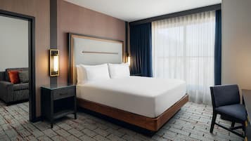 A hotel room with a large bed, a bedside table, a chair, a desk, a mirror, and a window with curtains.
