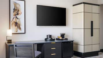 A hotel room with a desk, chair, a flat-screen TV, a coffee machine, and a wardrobe.