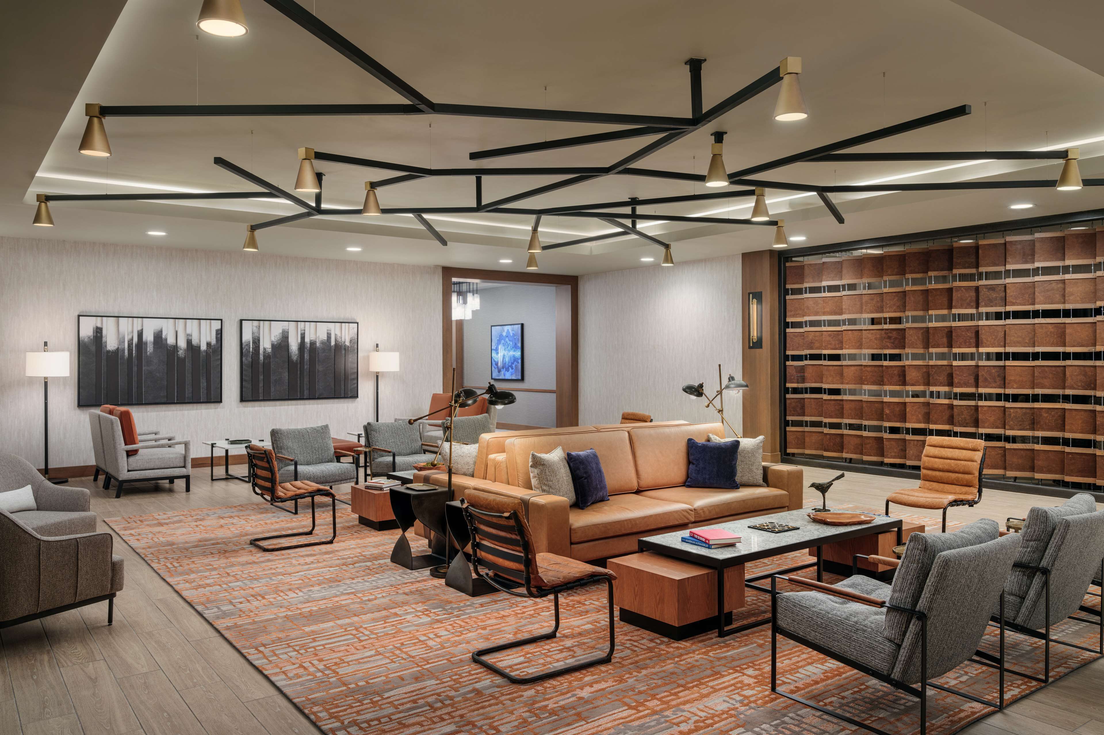 A modern hotel lobby with a leather sofa, armchairs, a coffee table, and a bookshelf.