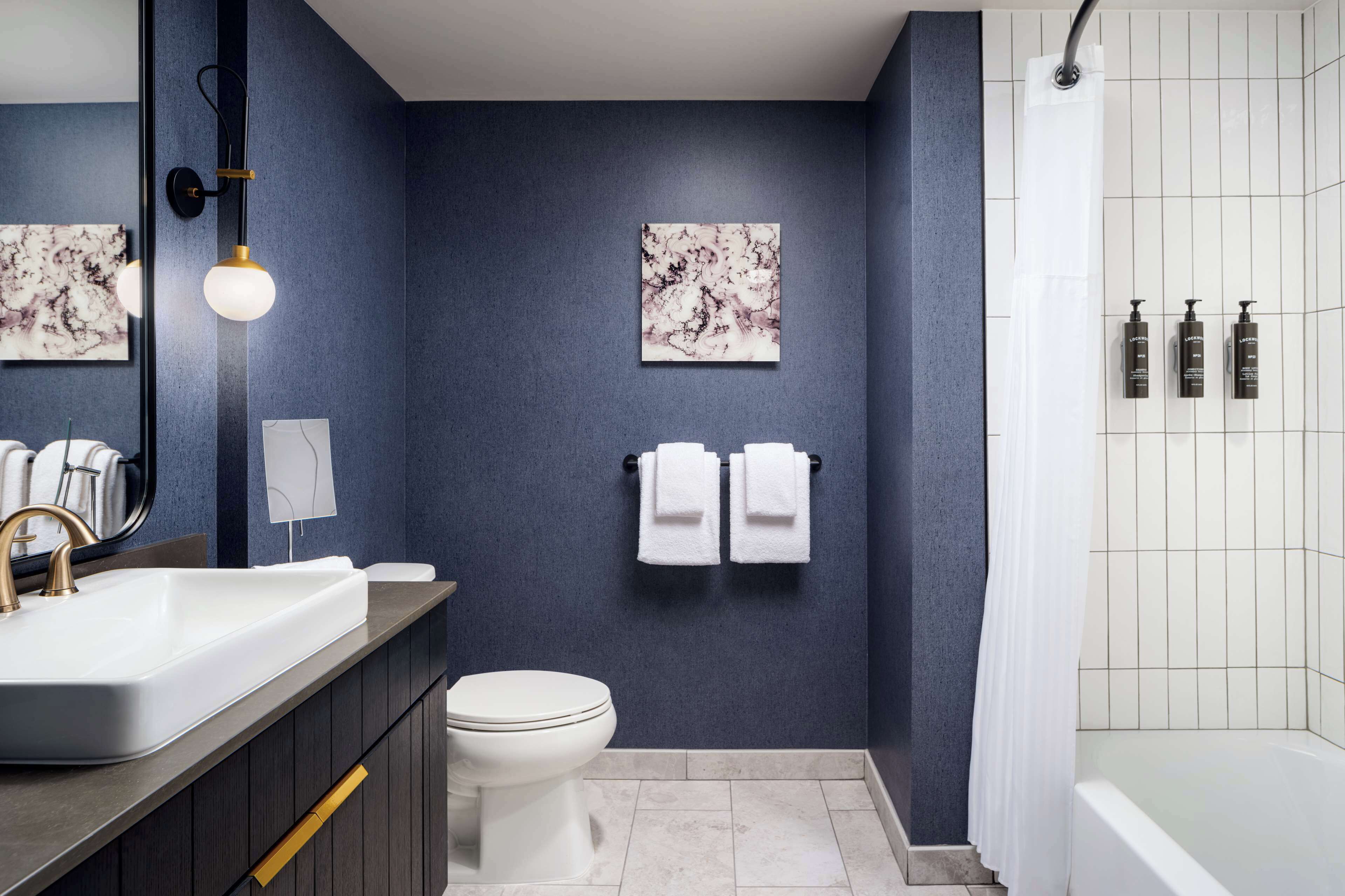 Un baño moderno con pared azul oscuro, un lavamanos blanco, un inodoro y una zona de ducha.
