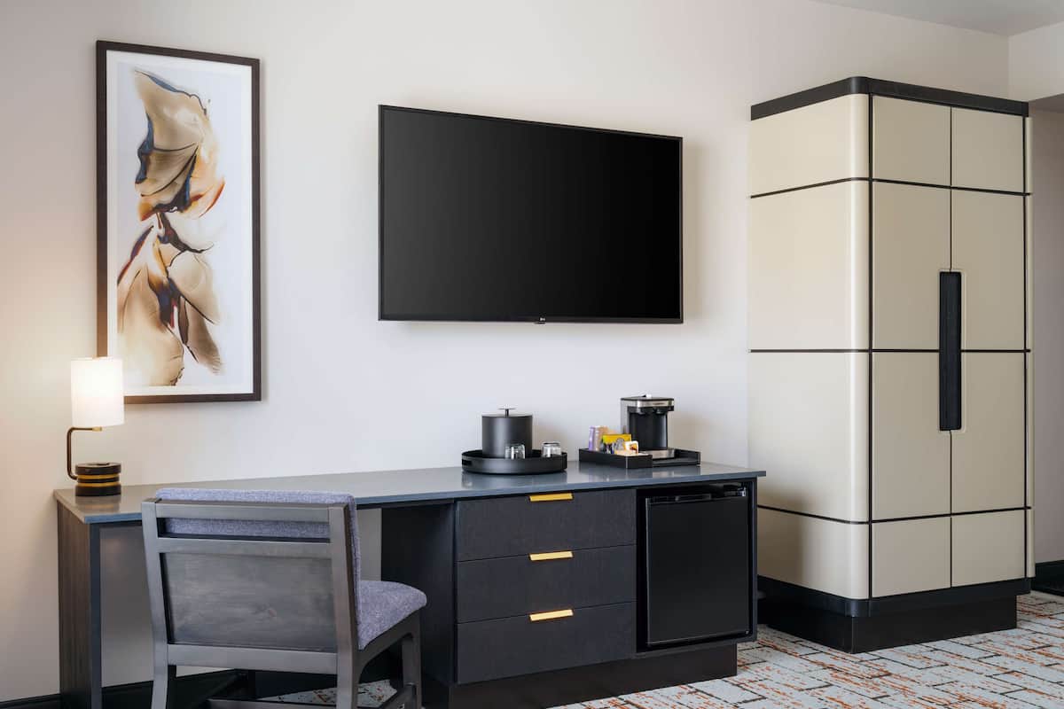 A hotel room with a desk, a flat-screen TV, a coffee maker, and a cabinet.