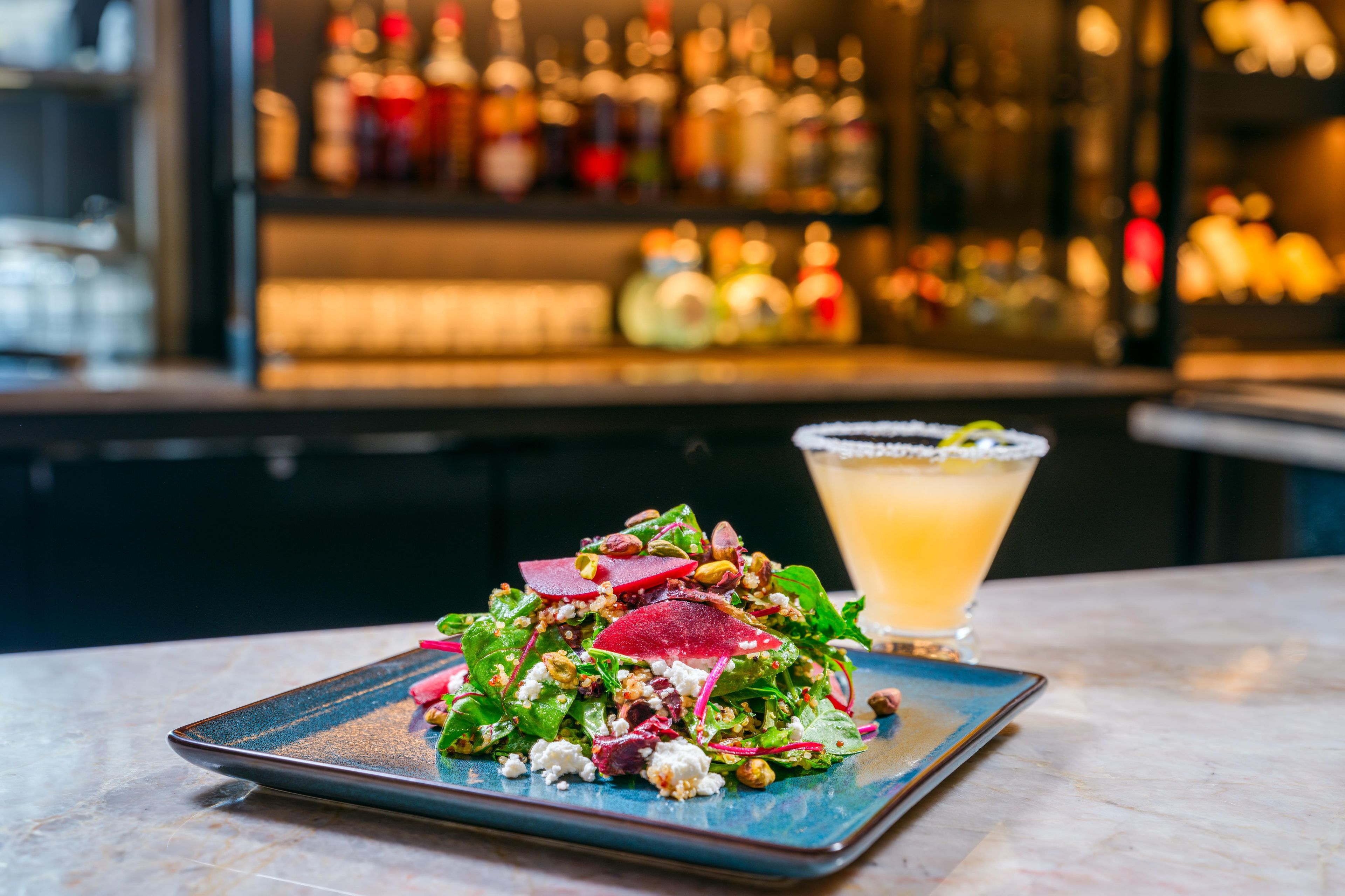 A plate of salad with a glass of drink on a table.