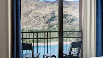 A balcony with two chairs and a table overlooking a mountainous landscape and a body of water.