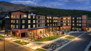 Un hotel moderno con varios pisos, mobiliario exterior y aparcamiento.