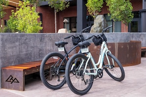 Two bicycles parked next to a bench in an outdoor area with a brick building and trees in the background. - The Hoffmann Hotel Basalt Aspen, Tapestry Collection By Hilton (Basalt)