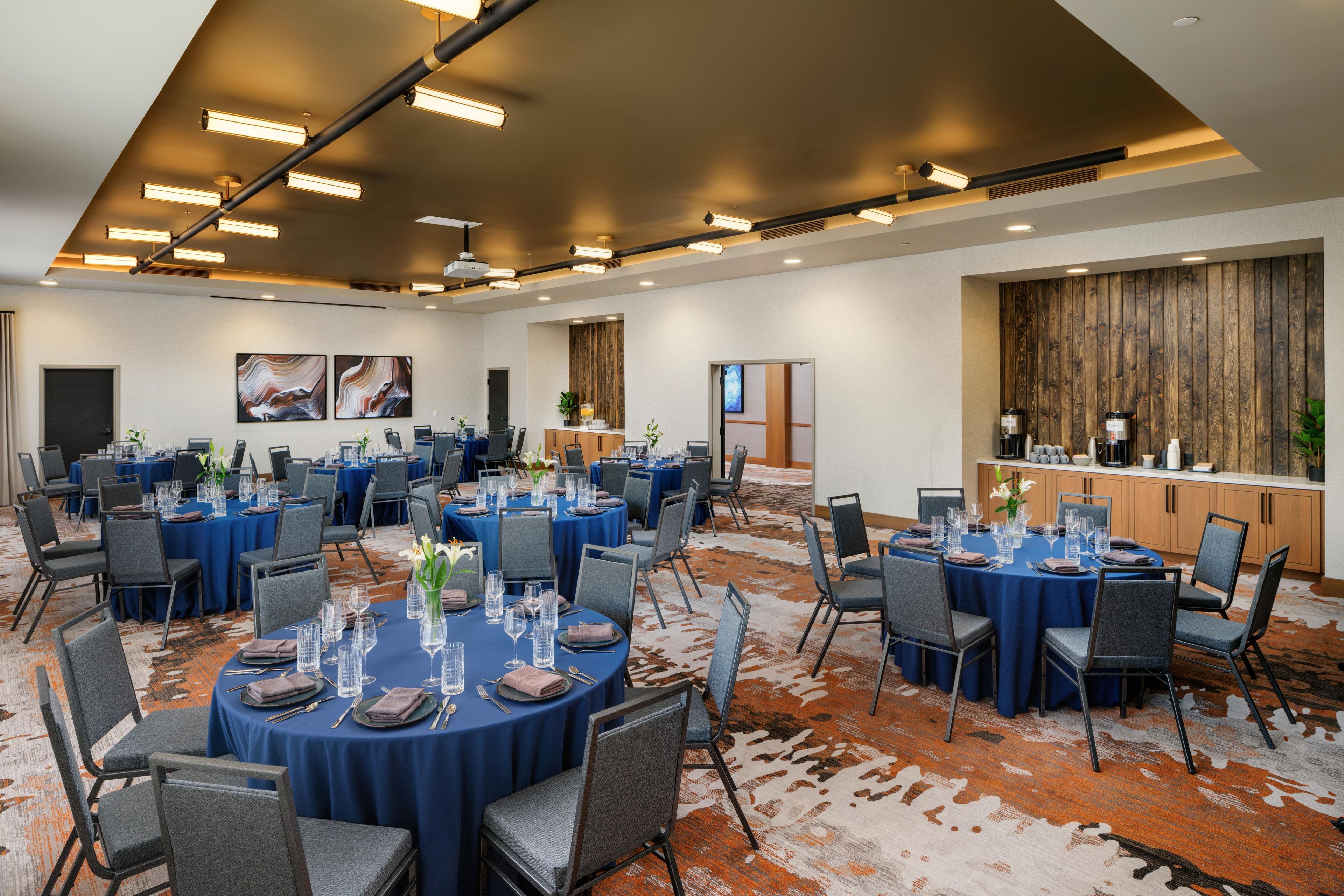 Sala de conferência com mesas redondas, cadeiras e espaço para buffet.