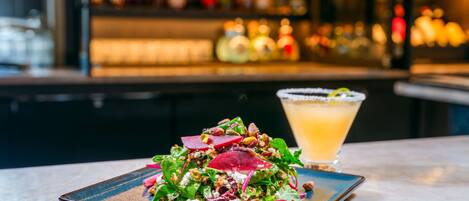 A salad on a plate with a drink in the background.
