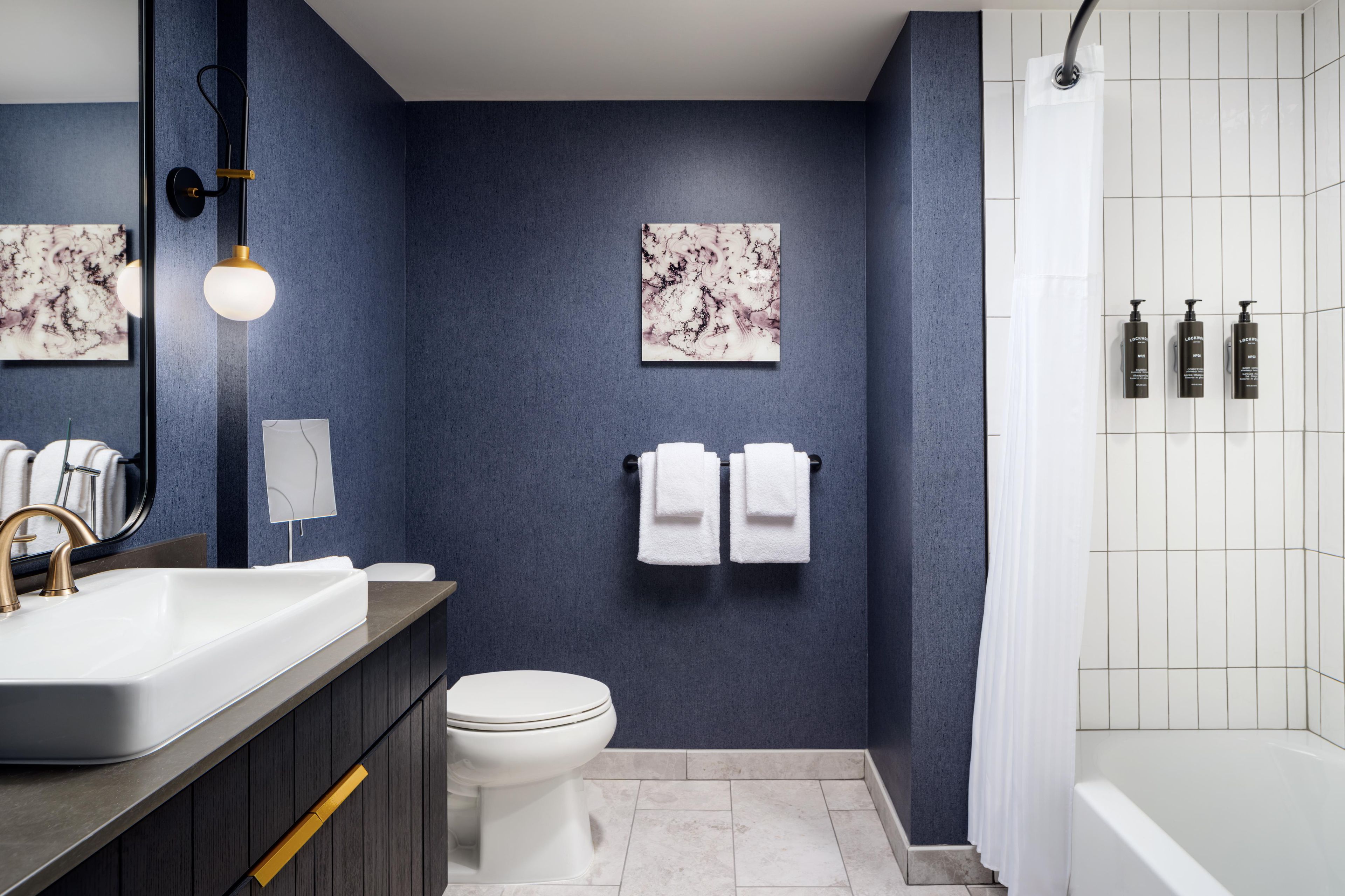 Een moderne badkamer met een donkerblauwe wand, een witte toilet, een wastafel met een gouden kraan, en een douchegedeelte met witte tegels.