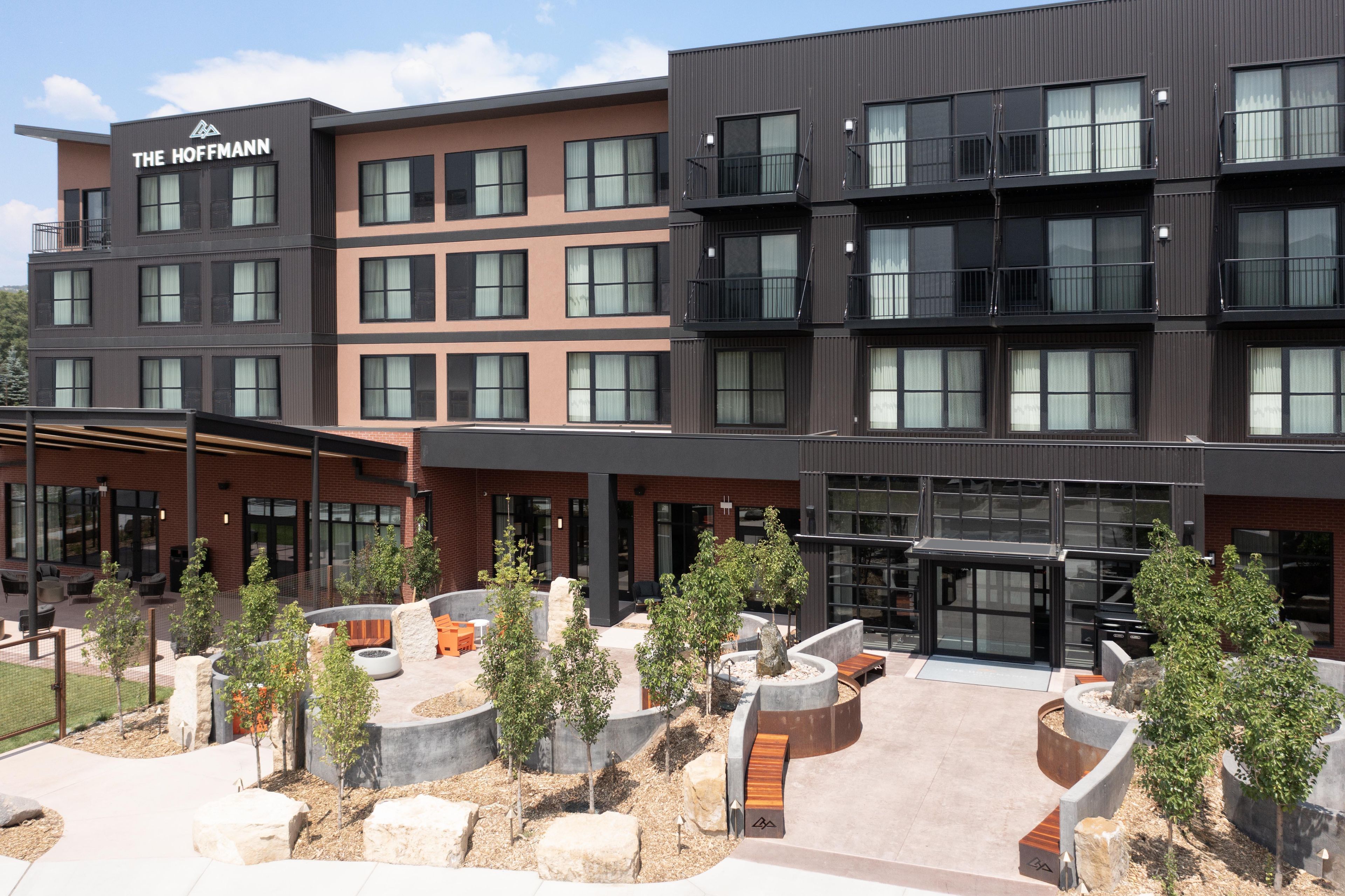 Un hotel de varios pisos con diseño moderno, que combina fachadas de ladrillo y metal, ventanas amplias y áreas de estar al aire libre con jardineras.