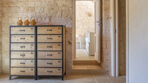 A stone-walled hallway with a wooden chest of drawers and wicker baskets.