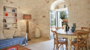 A cozy living room with a stone wall, a sofa, a coffee table, and a dining area with chairs and a table.