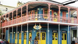Un bâtiment aux couleurs vives, sur lequel on peut lire l’inscription « DAT DOGS », et qui possède plusieurs portes portant les mentions « BOISSONS GAZEUSES », « COCKTAILS » et « BIENVENUE ! ».