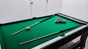 Une table de billard avec des billes et des queues, une porte blanche et un sol carrelé.
