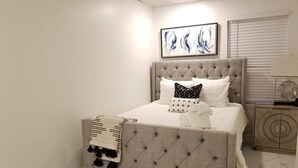 Une chambre à coucher avec un lit doté d’une tête de lit capitonnée, une literie blanche et un plaid décoratif.