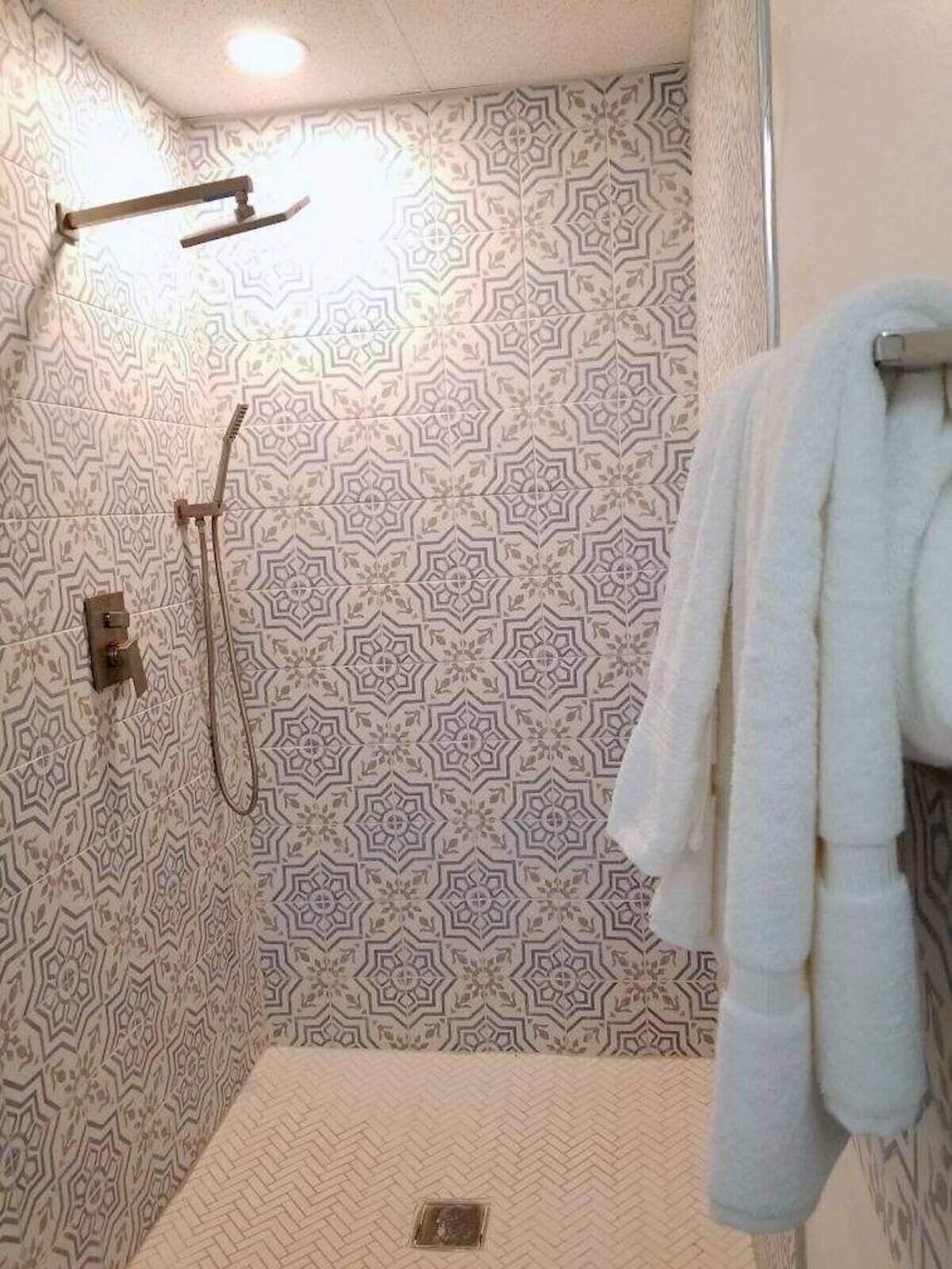 A shower area with patterned tiles, a handheld showerhead, and a towel rack with towels.