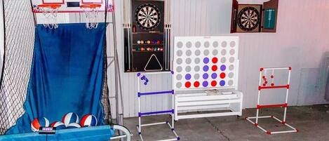 Un espacio recreativo con un aro de baloncesto, dardos, un dardo con puntos de colores y una pequeña mesa.