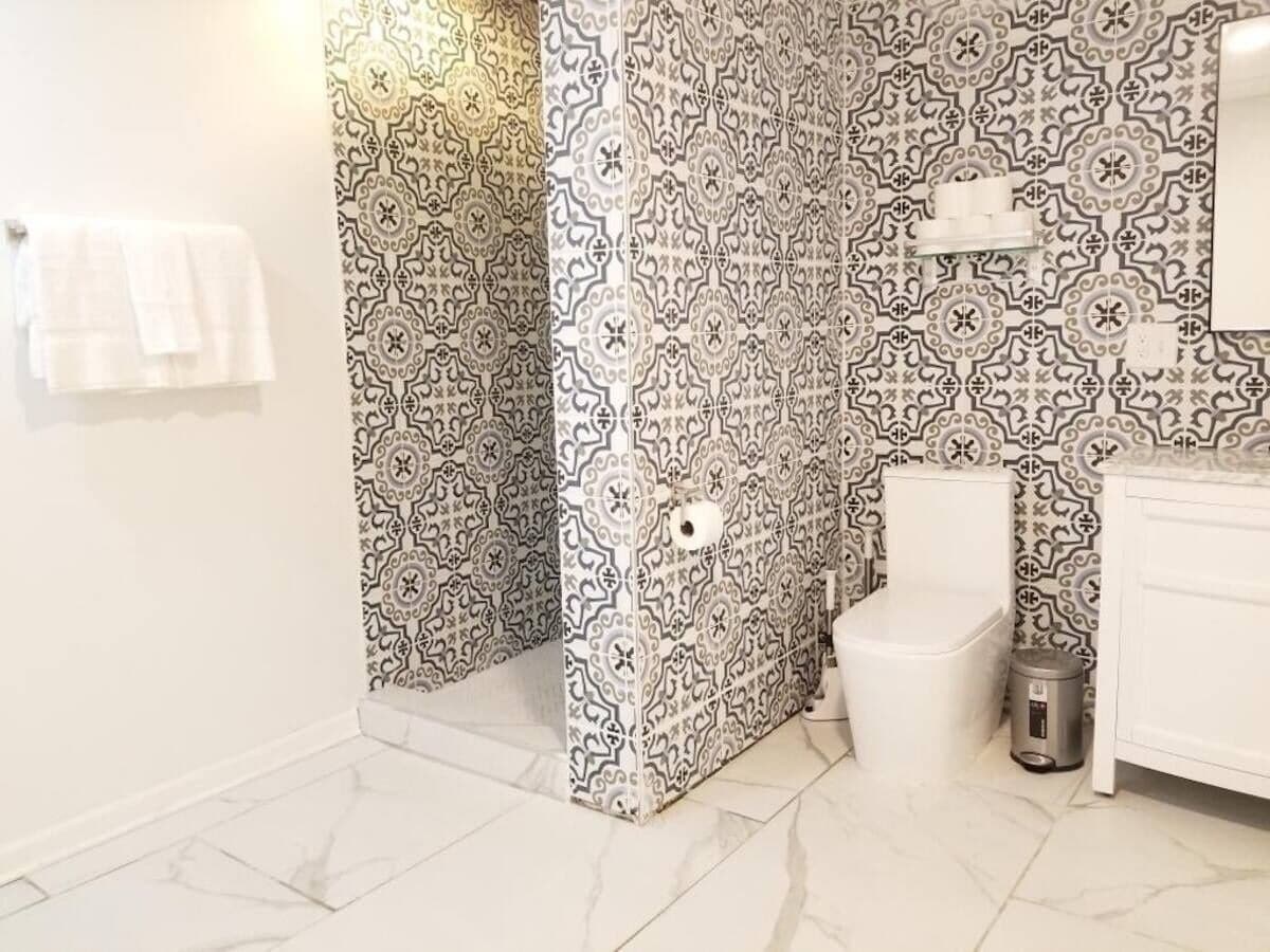 A bathroom with patterned tiles, a toilet, a sink, and a trash bin.