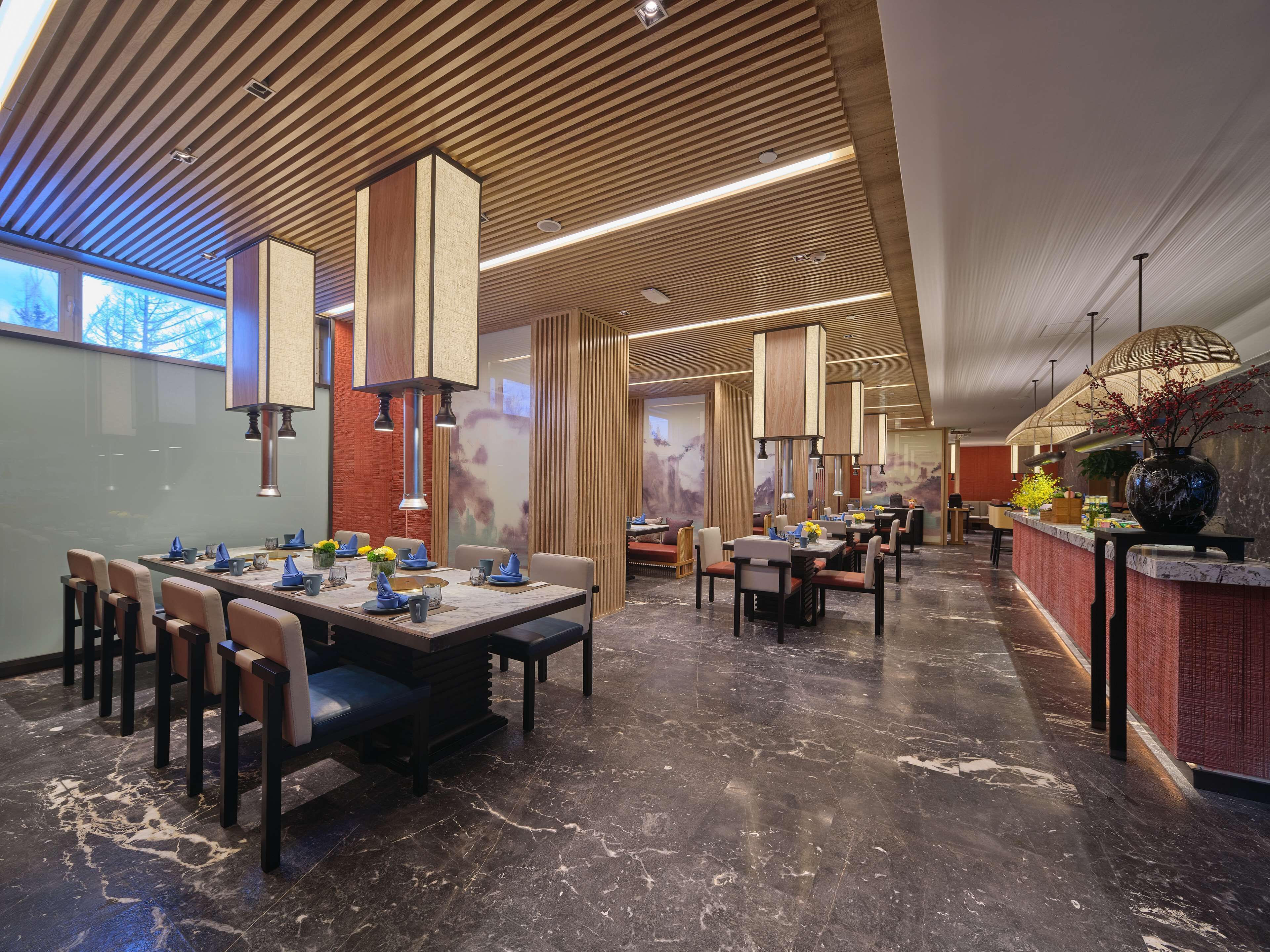 Un restaurante moderno con techo alto, paneles de madera y piso de mármol.