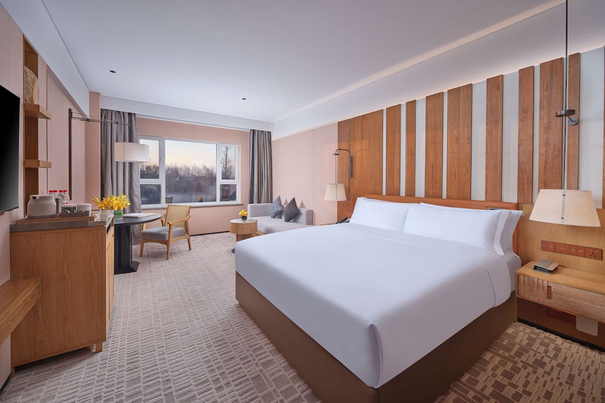 A hotel room with a large bed, a desk with a chair, a television, and a window with curtains.
