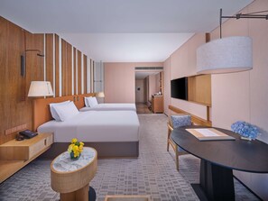 A hotel room with two beds, a desk, a chair, a TV, and a bathroom visible in the background.