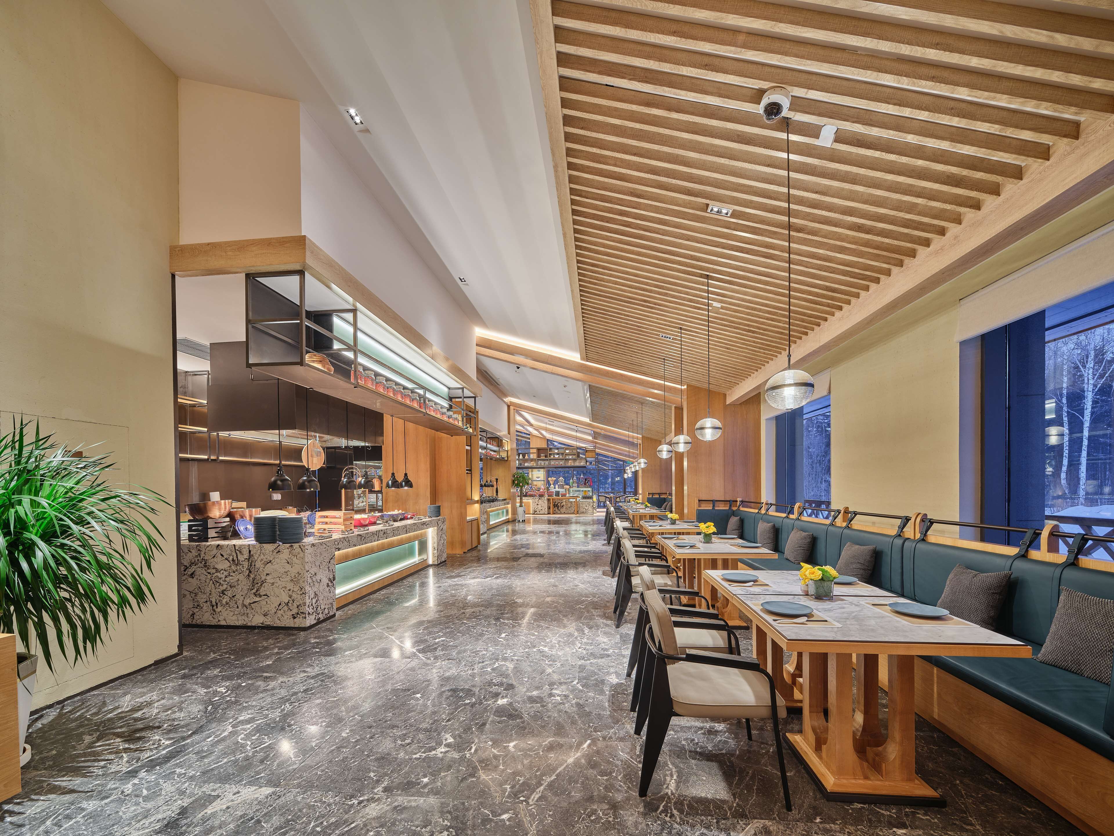 A modern restaurant interior with marble flooring, wooden ceiling beams, and seating areas with tables and benches.