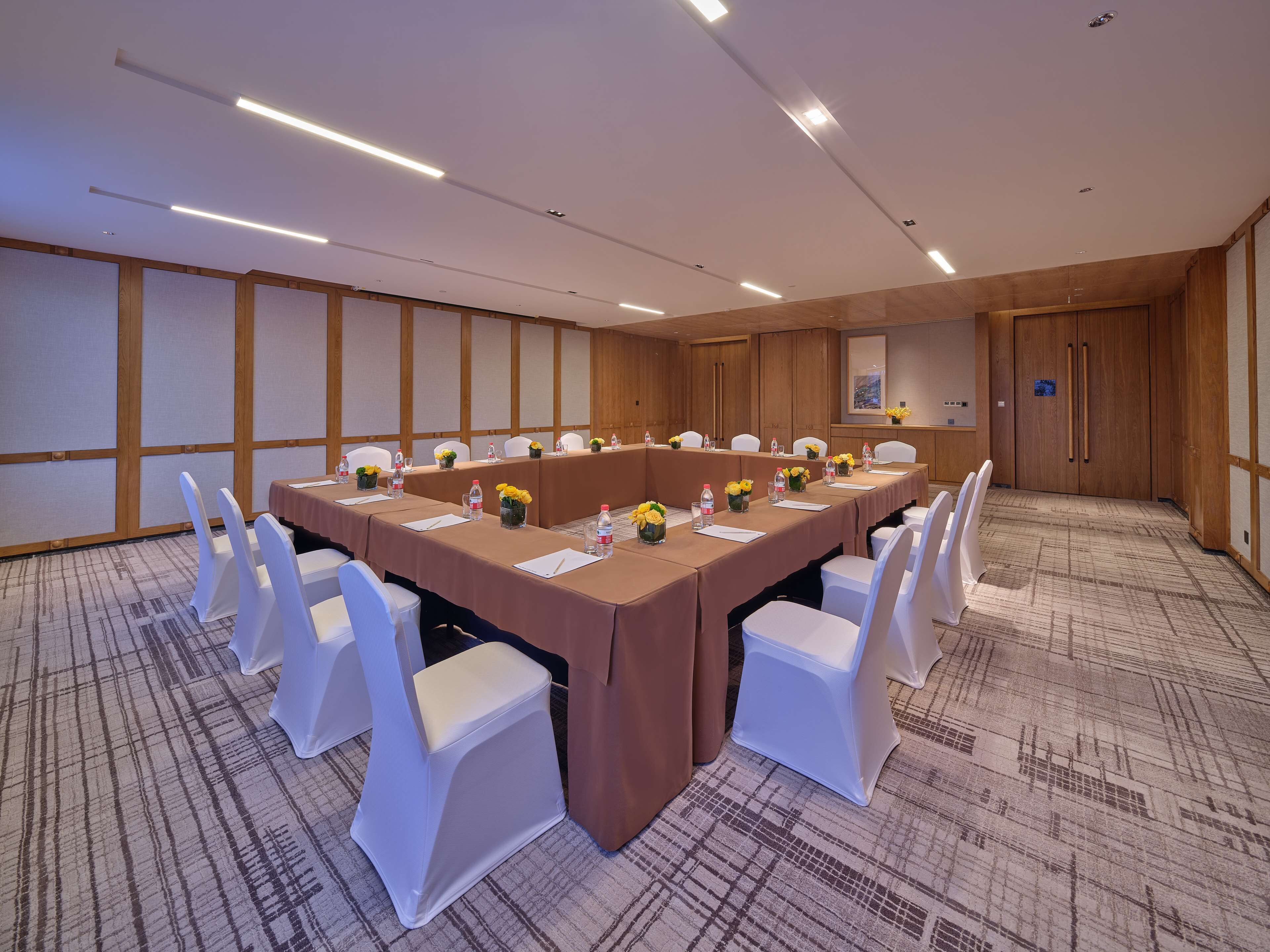 A conference room with a long table, white chairs, and floral centerpieces.