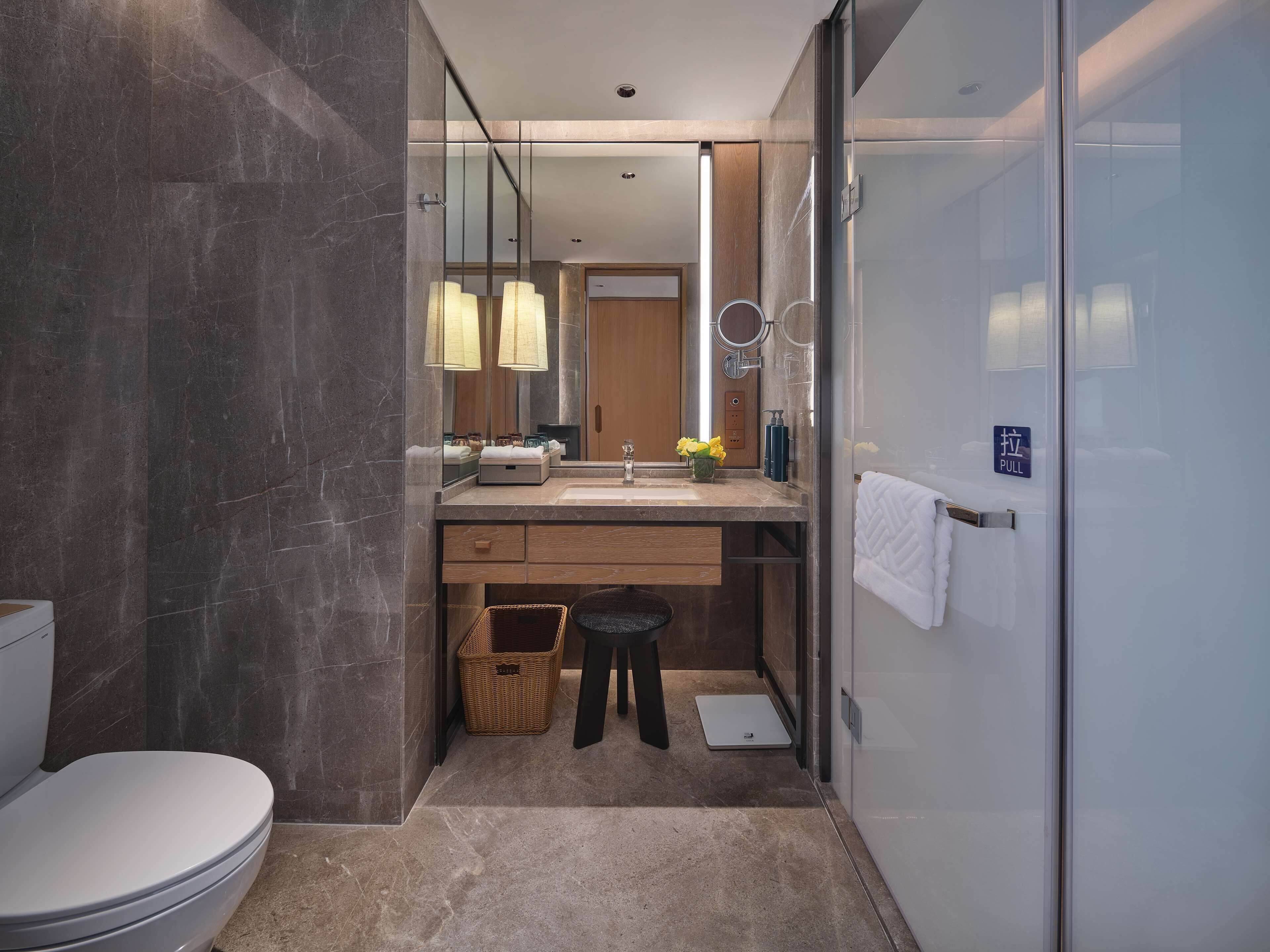 A modern bathroom with a glass shower enclosure, a wooden vanity, a white toilet, and a small wicker basket.