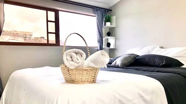 Un lit bien fait, avec du linge de lit blanc et un panier rempli de serviettes pliées posé sur le lit.