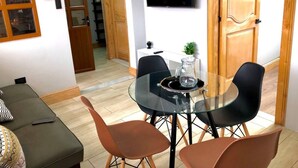 Un salon moderne avec une table à manger en verre, des chaises noires, un téléviseur affichant le logo « NETFLIX » et un coin salon confortable avec un canapé et des coussins.