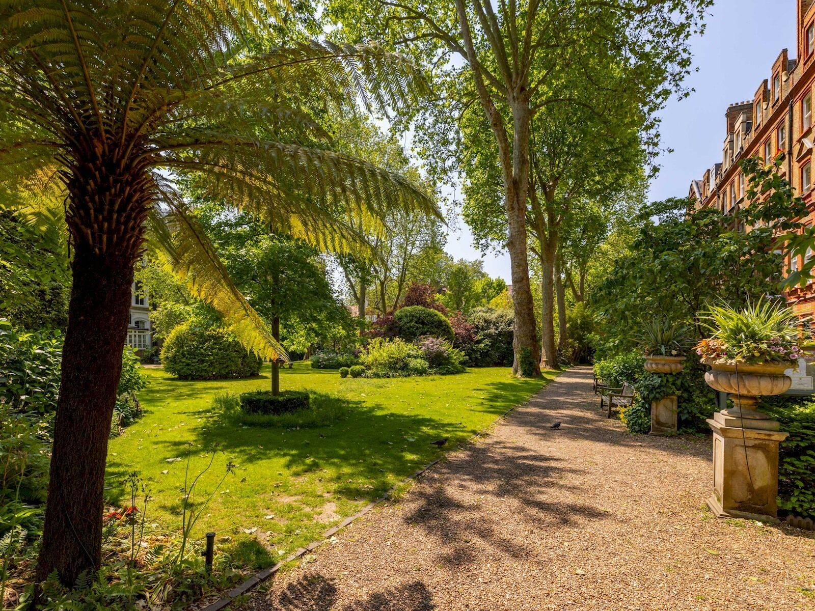 A garden pathway flanked by lush greenery and a building with a classic architectural style.