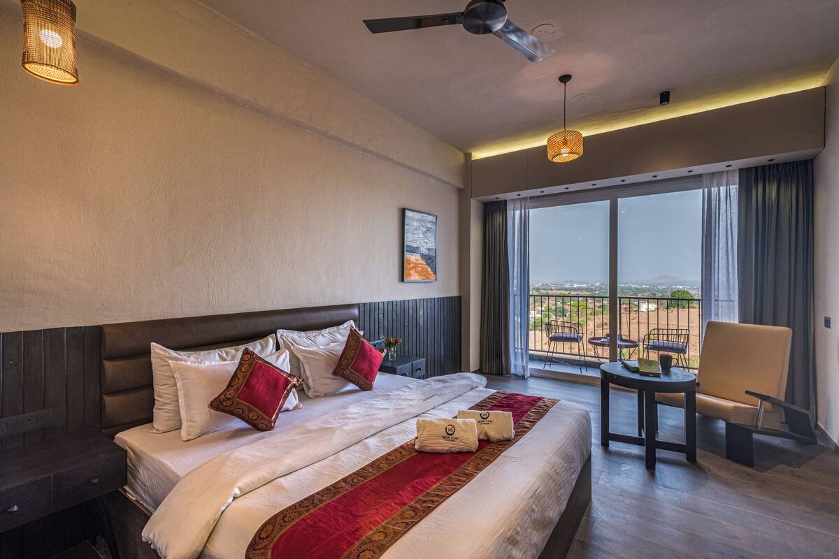 A hotel room with a large bed, a desk, a chair, and a balcony with a view.