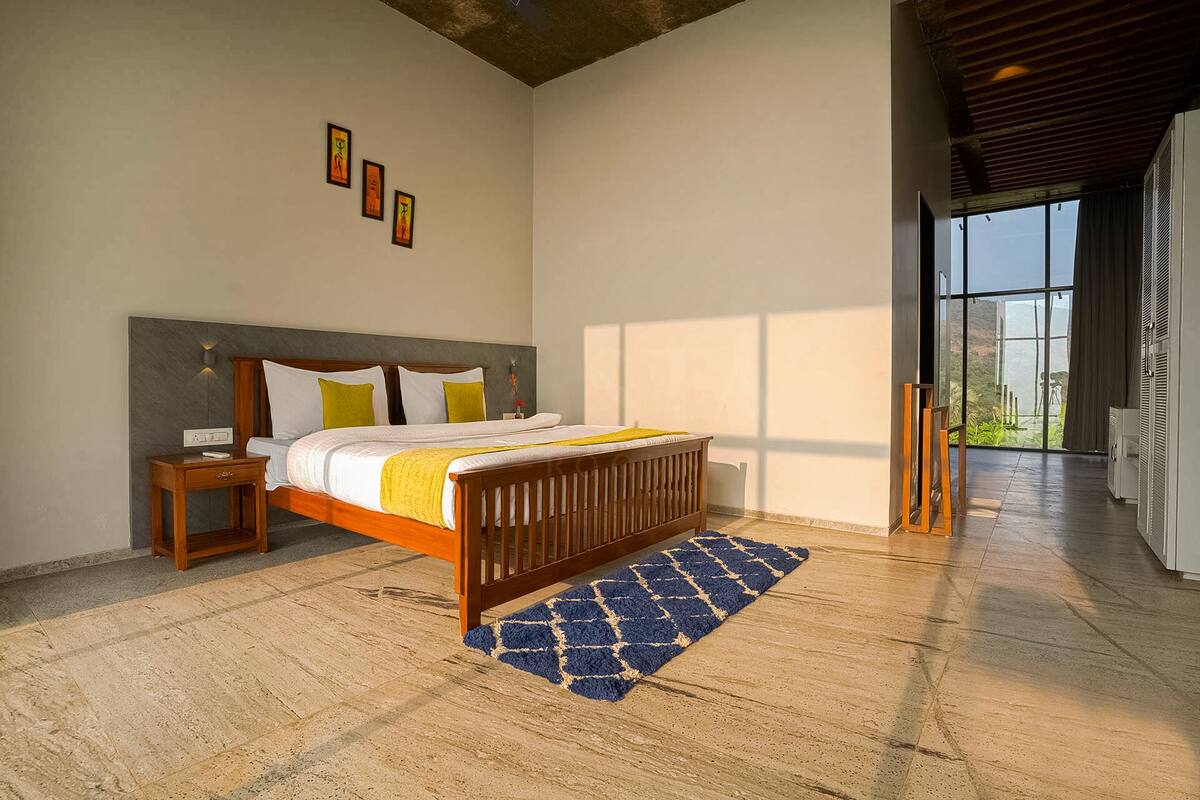 A modern bedroom with a wooden bed, a nightstand, and a large window offering a view of the outdoors.