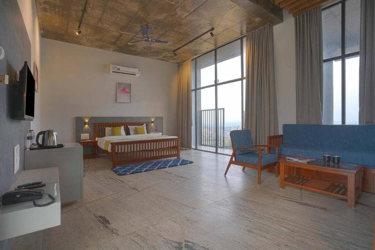 A hotel room with a bed, a sofa, a coffee table, a TV, and a balcony with curtains.