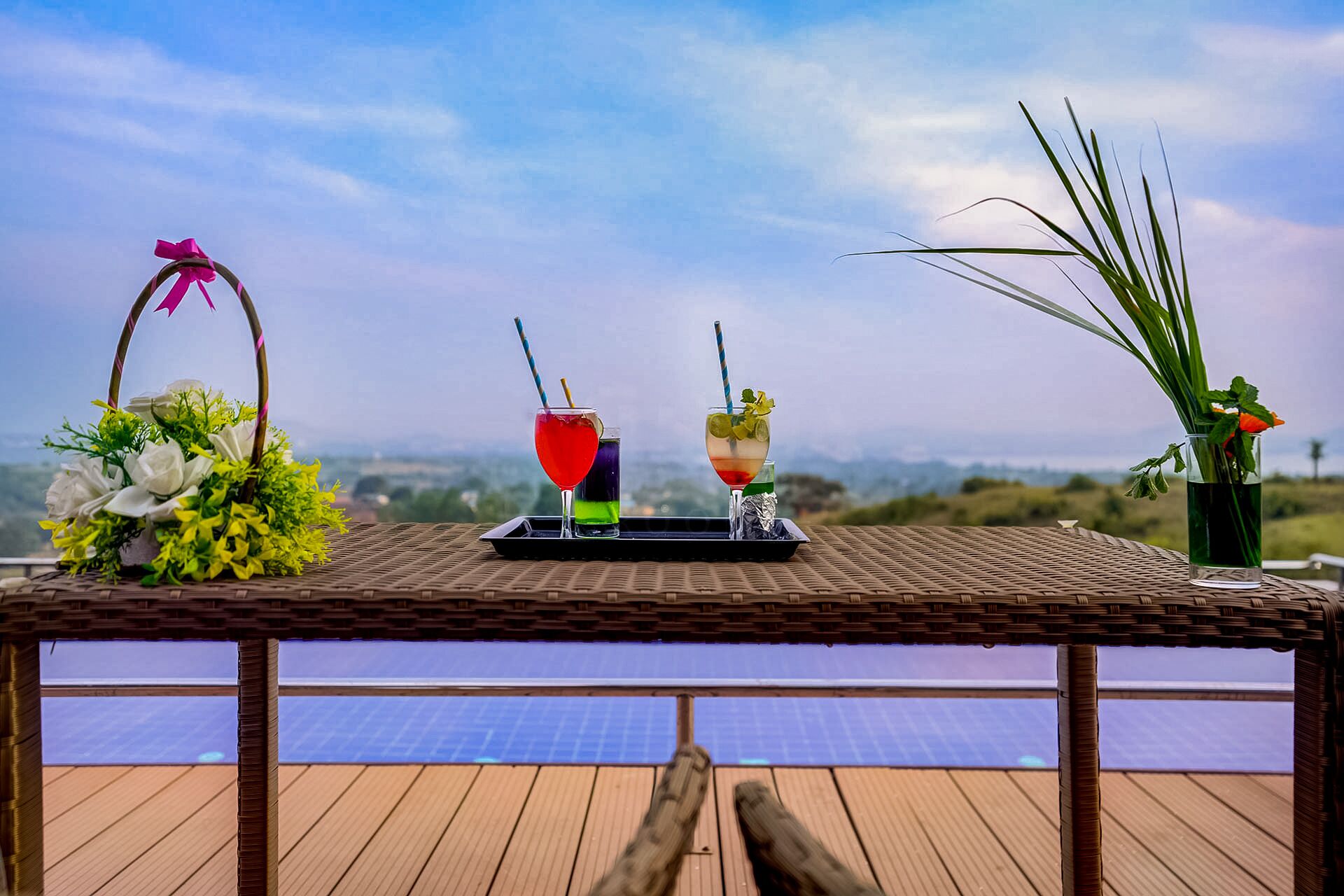 A table with drinks and a floral arrangement on a deck with a view of the landscape.