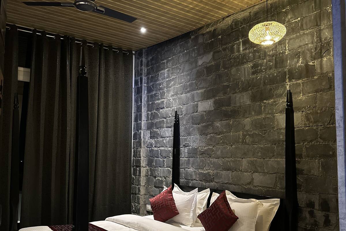 A modern bedroom with a large bed, dark curtains, a ceiling fan, and a brick wall.