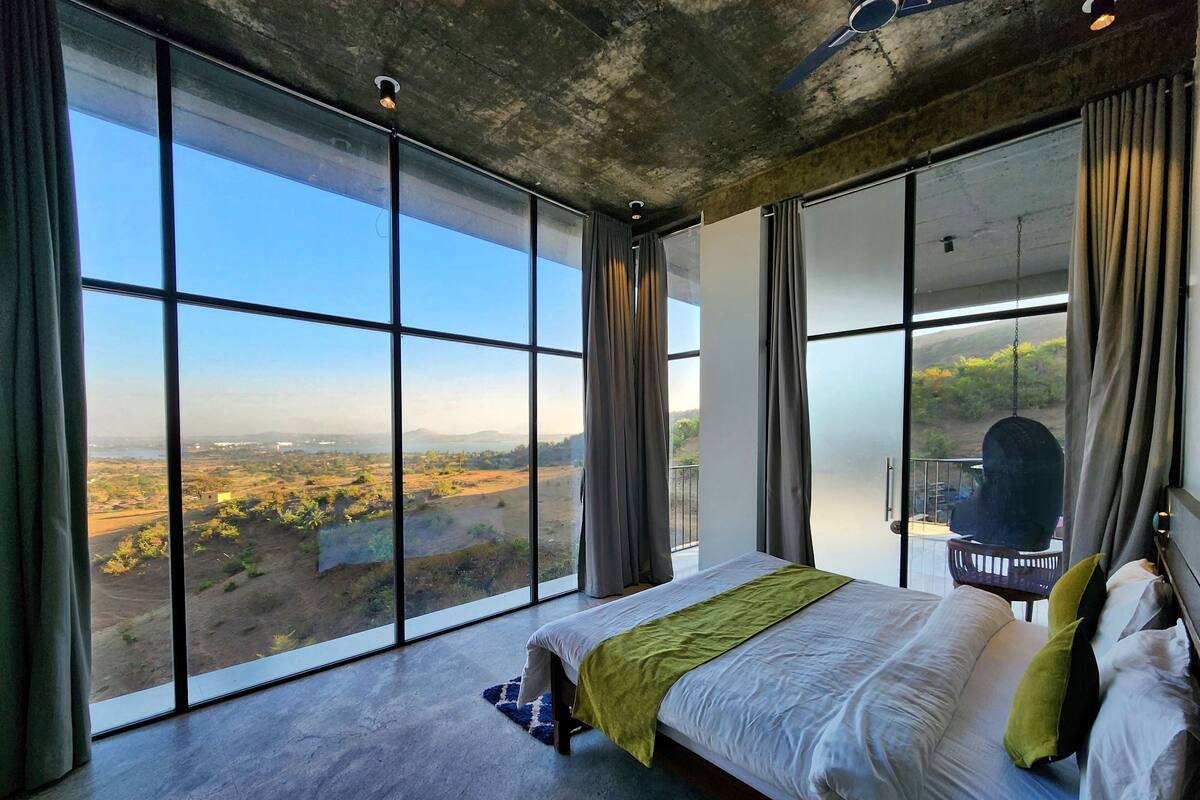 A bedroom with a large window, a bed, and a view of a landscape.
