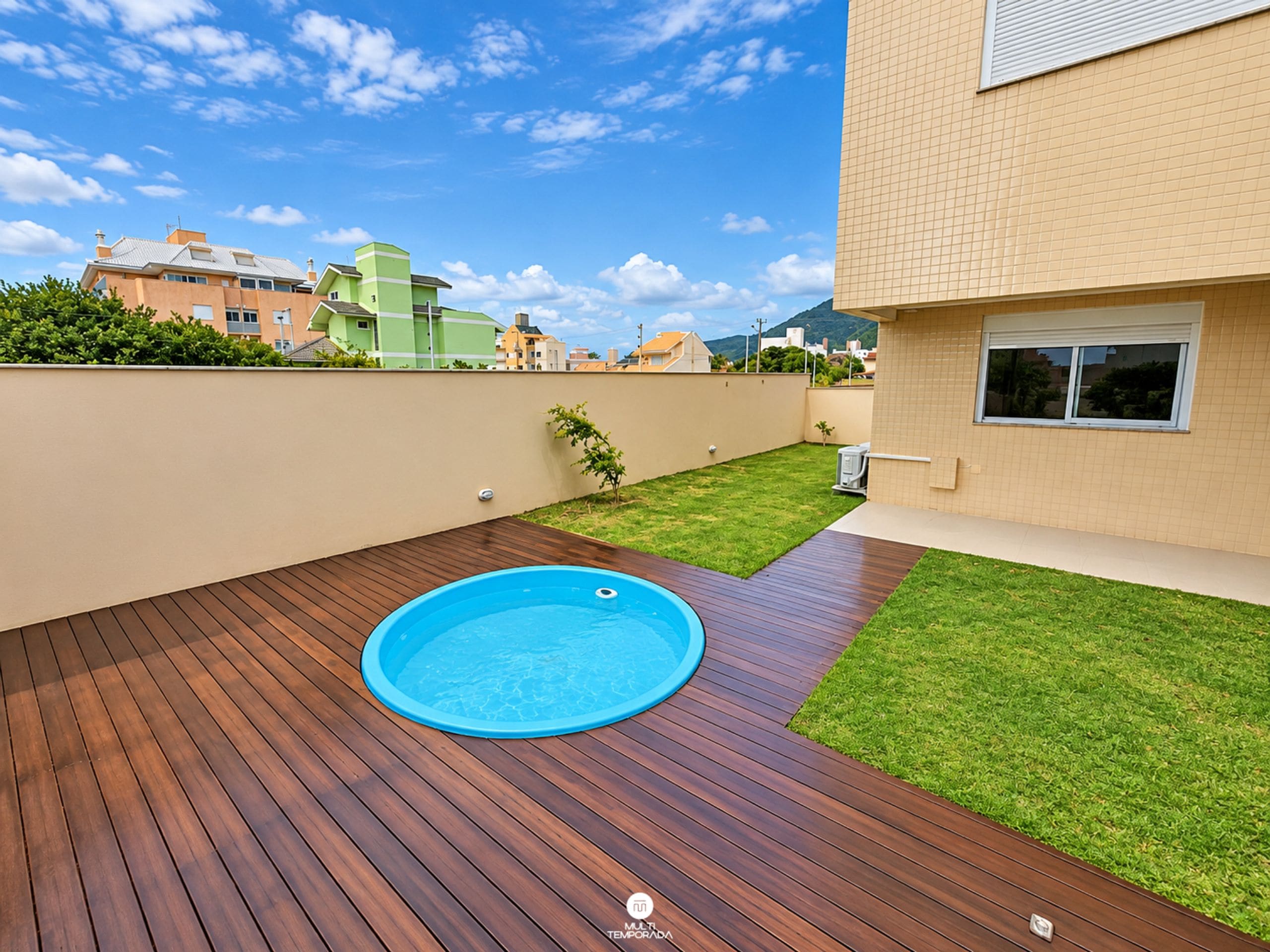 A swimming pool on a wooden deck with a small grassy area and a wall.